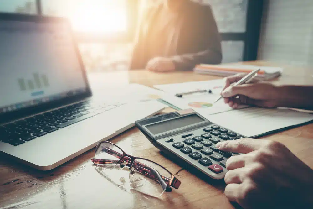 A Saskatchewan resident, who happens to be an RV Park owner, diligently works at a desk using a calculator and a laptop.