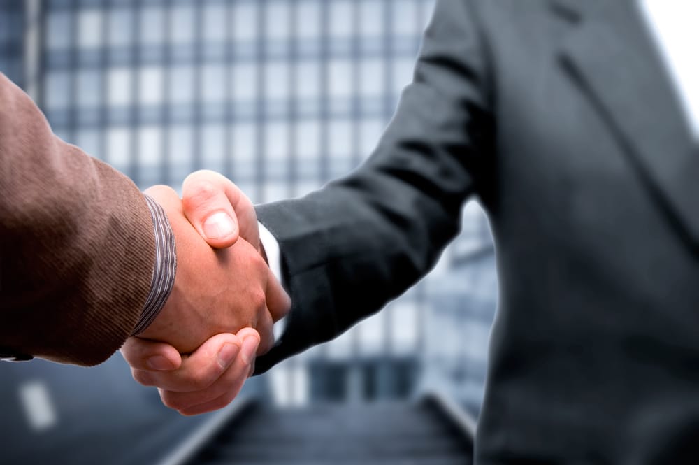 Two businessmen shaking hands in front of a building at Scott Motor Coach Sales.