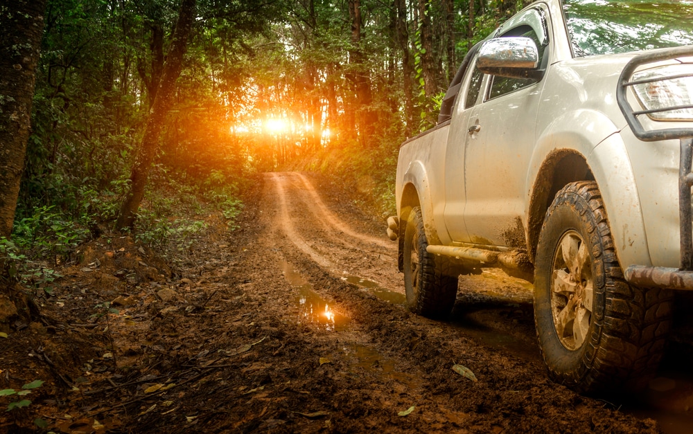 A white pickup truck from the Off-Highway Motor Vehicle Recreation Division driving down a muddy road in the forest.