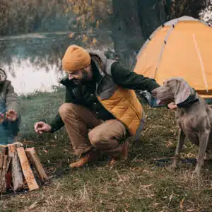 A couple with a dog enjoying a campfire together.