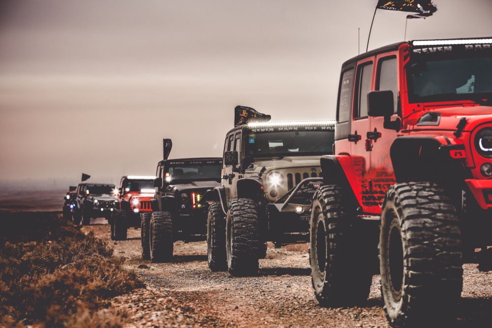 A line of red jeeps on a dirt road at the California Off-Highway Vehicle Rec Area, as volunteers from BLM oversee the activity.