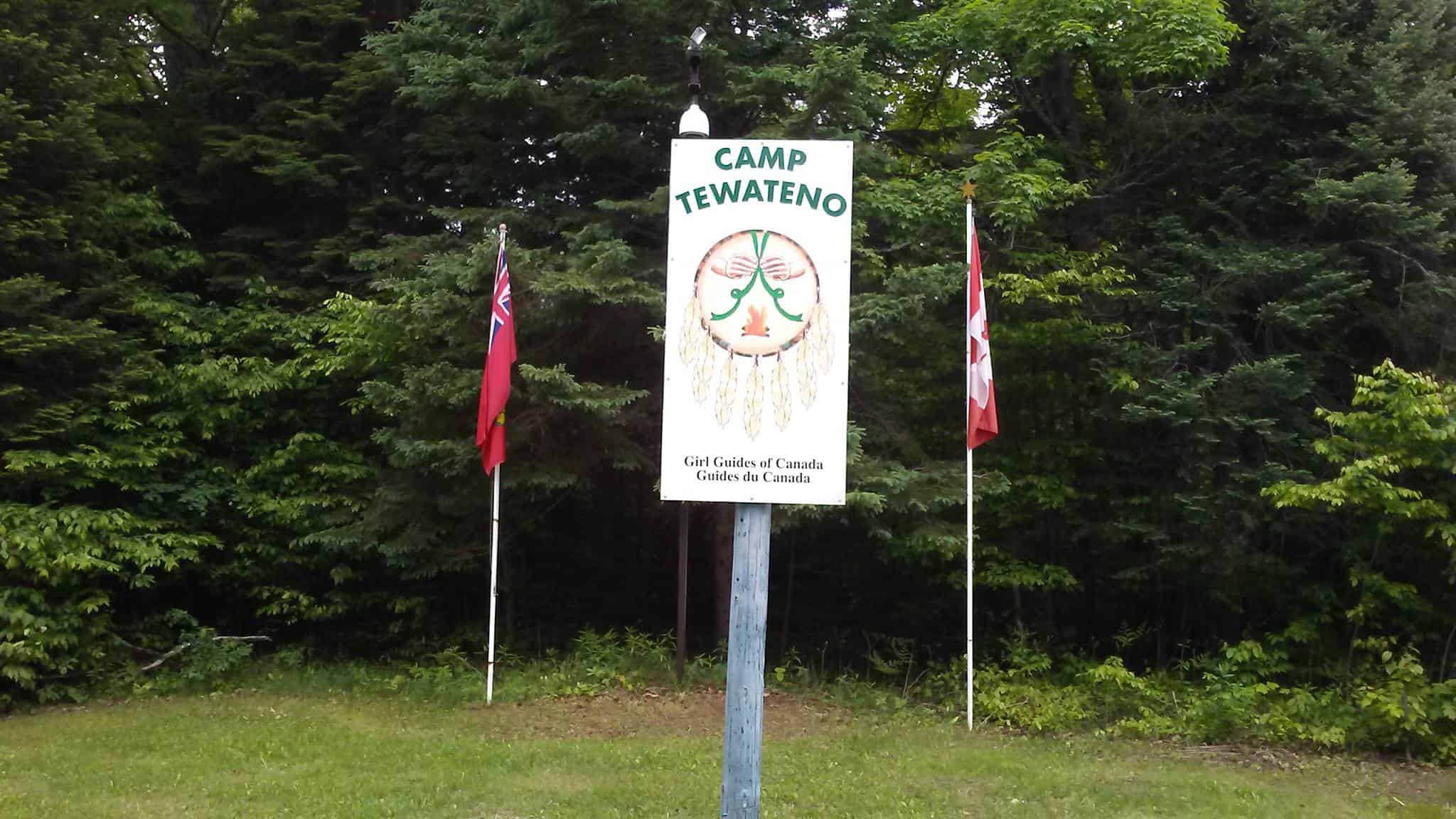 A sign with two flags in front of a grassy area at a local club.