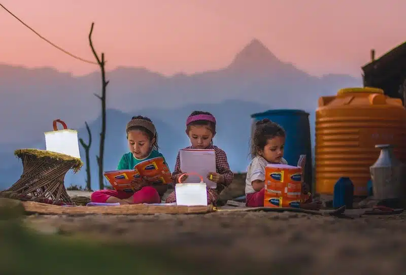 Three young girls reading books in front of a tent in Nepal, showcasing Adventure Ready Brands.