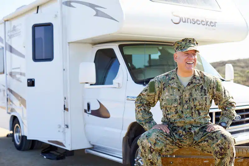 A veterans day tribute featuring a man in military uniform sitting in front of an outdoorsy RV.