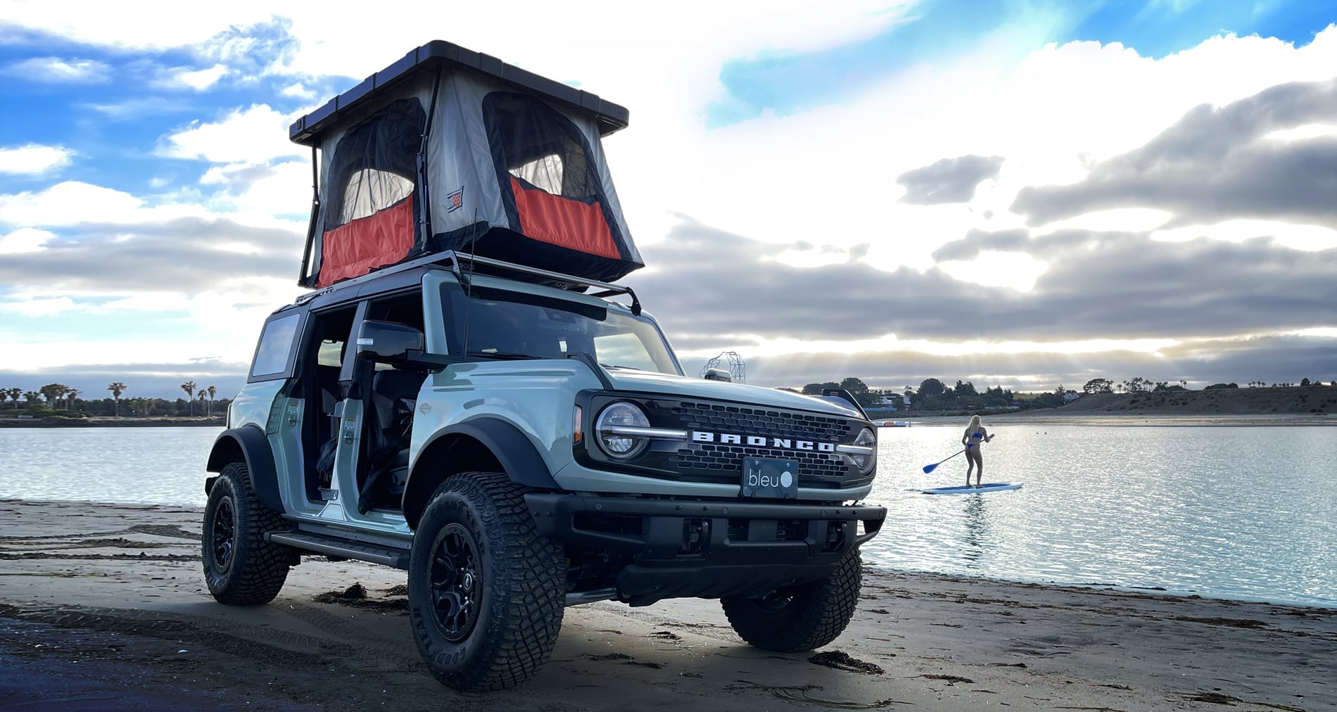 A jeep with the Latest Rooftop Tent on top of it near the water.