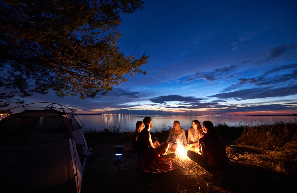A group of friends sitting around a colorful fire pit at night.