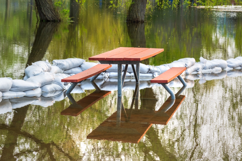 A picnic table sits on top of sandbags in a flooded area.