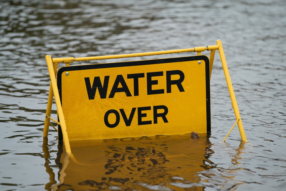 A yellow water over sign in a flooded area.