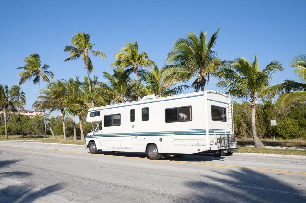 An RV, provided by Lazydays, is seen traveling down a road in Florida with palm trees lining the background.