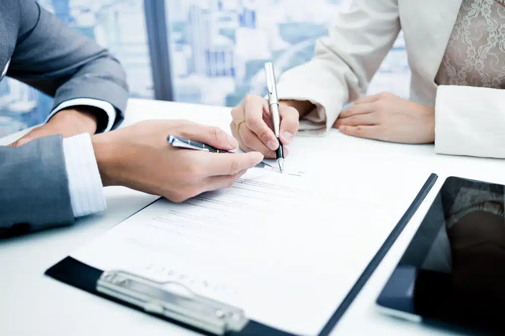 Two business people from Patrick Industries and Wet Sounds signing an acquisition document at a desk.