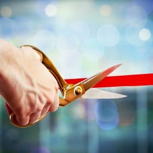 A person cutting a red ribbon with a pair of scissors.