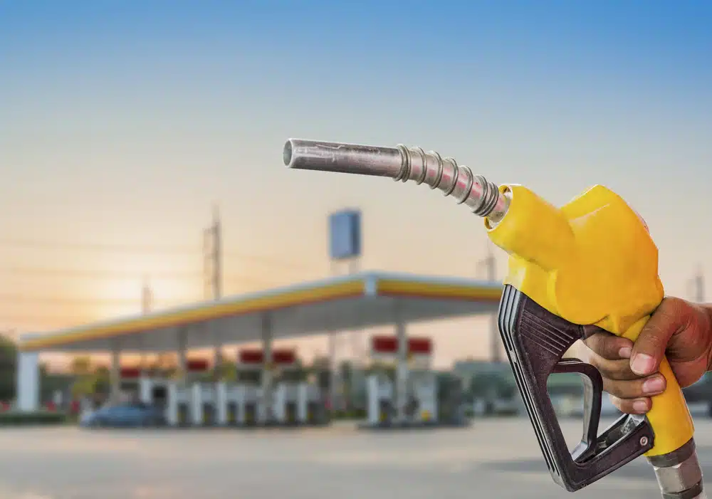 A man holding a yellow gas nozzle at a gas station, as the national average for gas dips.