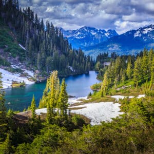 A scenic mountain lake nestled amidst towering trees and glistening snow, showcasing the natural beauty that can be preserved through National Park System protection.