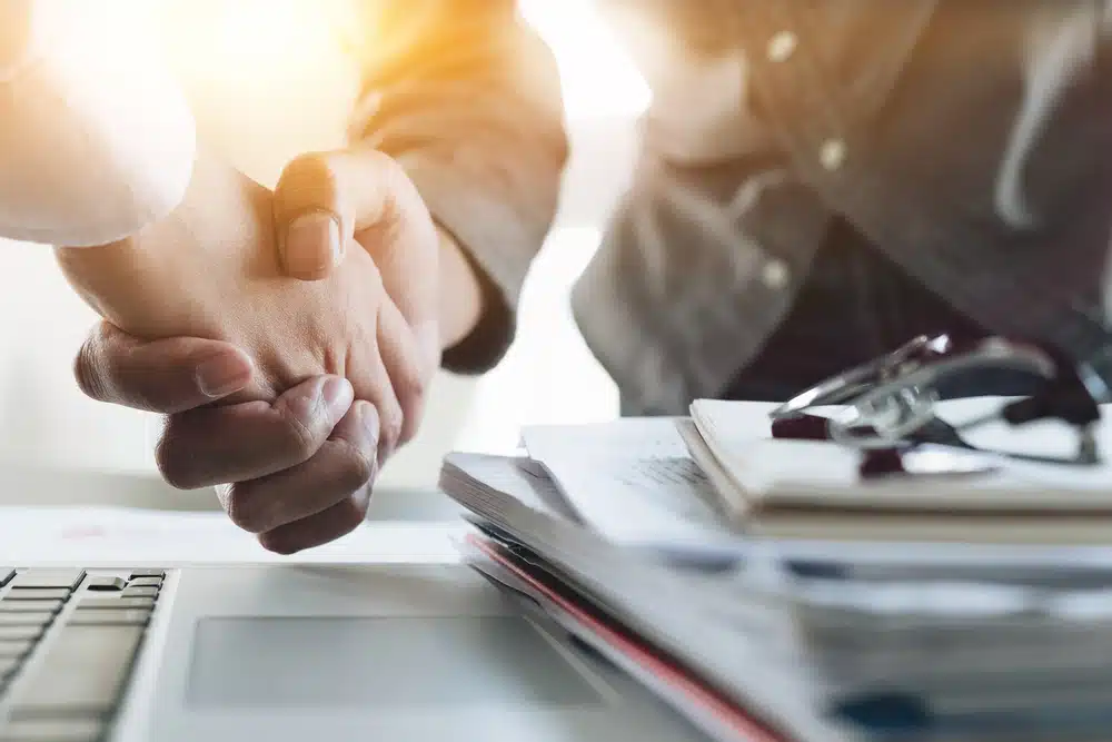 Two business people shaking hands in front of a laptop at Park Holidays UK.