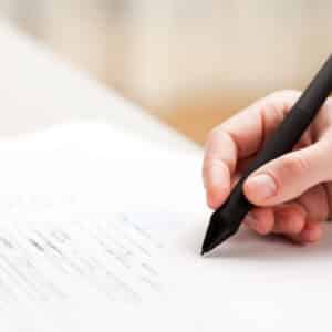 A person signing a document with a pen.