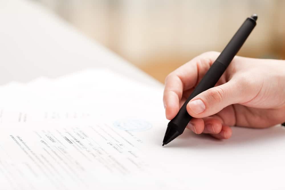 A person signing a document with a pen.