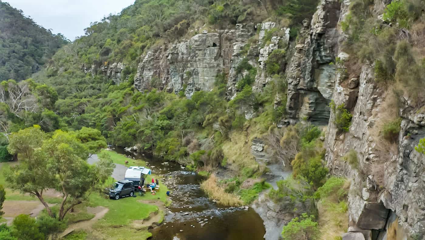 An aerial view of an RV parked next to a river, showcasing the ProSmart App for remote control and monitoring with BMPRO updates.