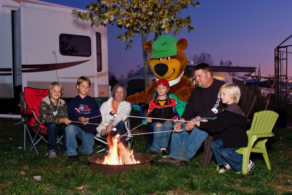 A family sits around a campfire with a teddy bear at Sun Outdoors.