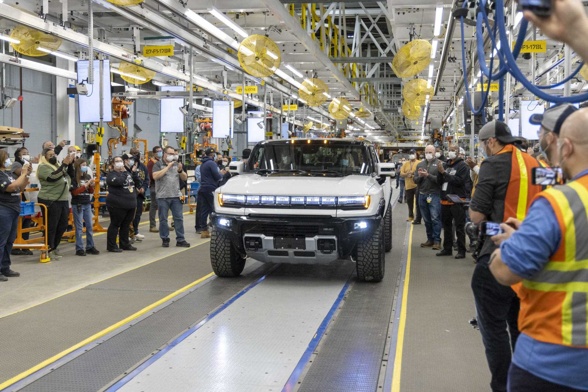 A group of people are taking pictures of a General Motors off-road supertruck in a factory.