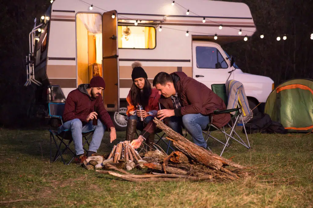 A group of people sitting around a campfire in front of an rv.