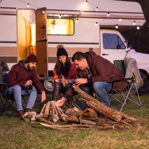 A group of people sitting around a campfire in front of an rv.