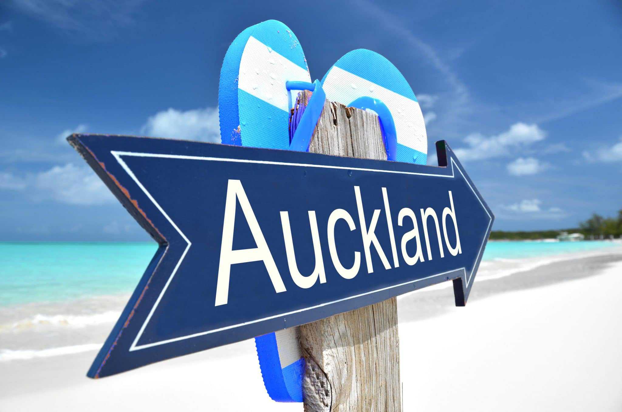 A sign pointing to Auckland on a beach.