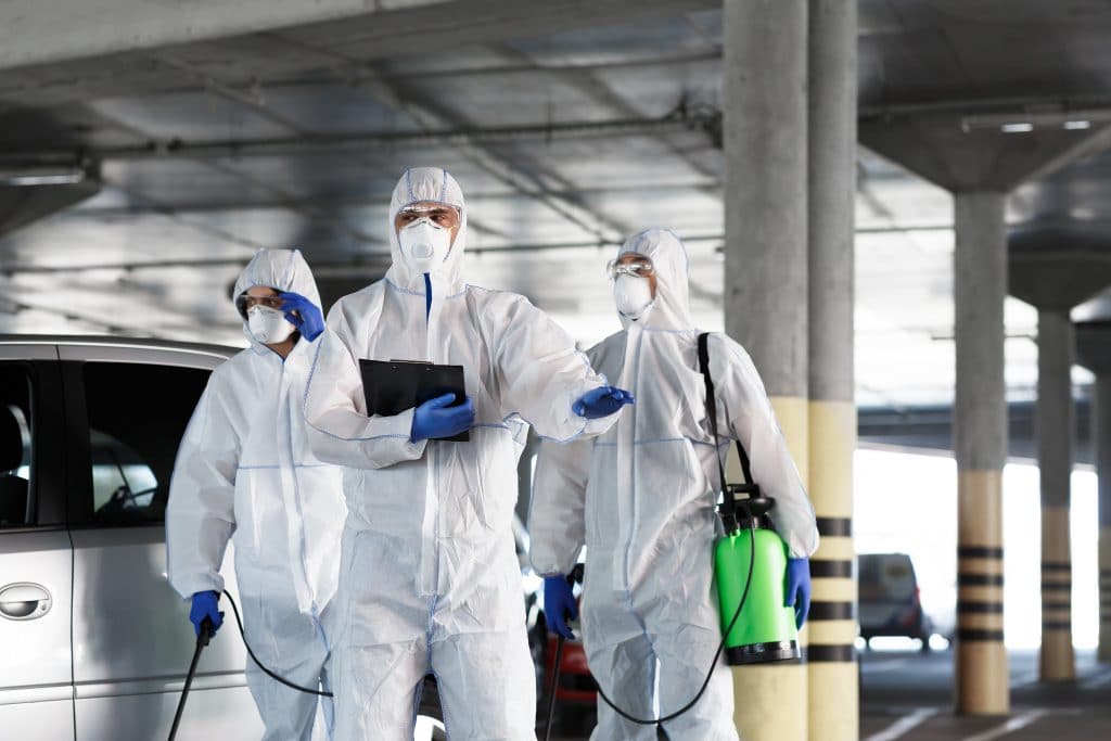 Three Tourism Operators in protective suits standing next to a car in a parking lot.