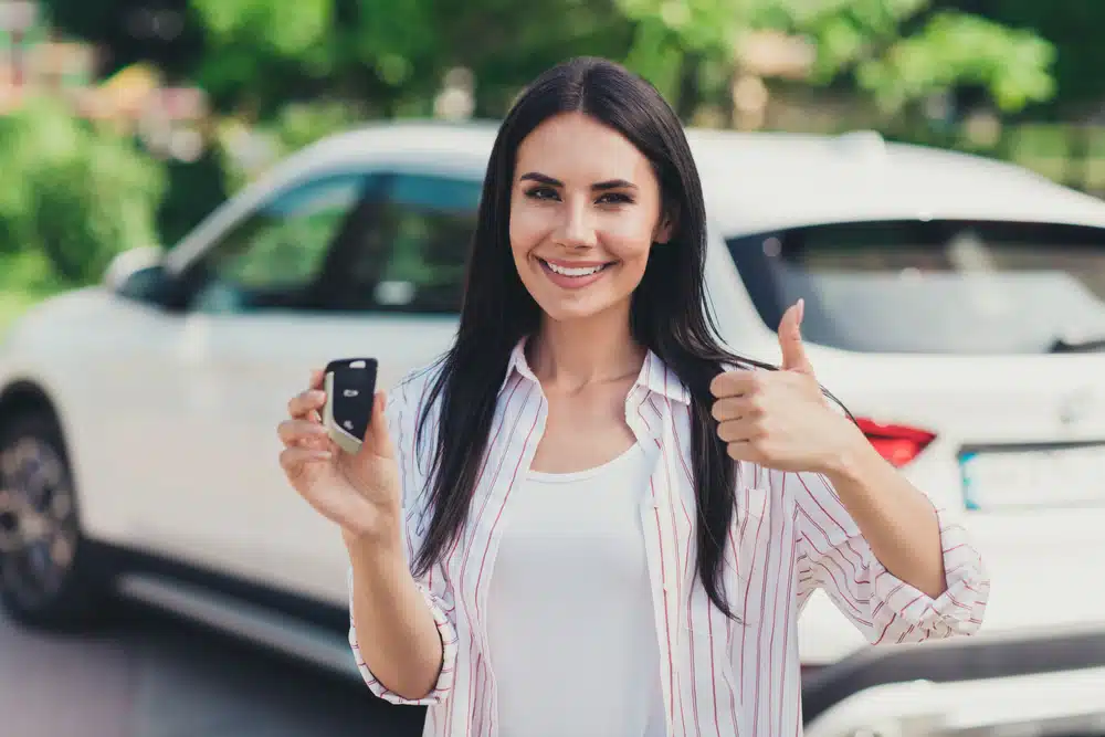 A Millennial woman proudly displaying her new car keys in front of a white pickup truck.