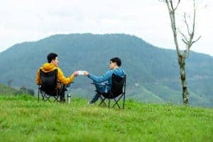 Two people sitting in a folding chair on a grassy hill at an inclusive glamping site near Seoul.