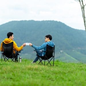 Two people sitting in a folding chair on a grassy hill at an inclusive glamping site near Seoul.