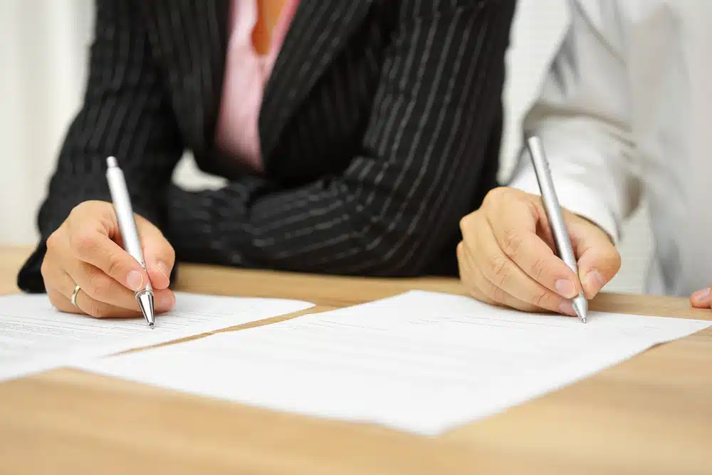 Two business people, representing Global Electric Trailer Systems and ZF Friedrichshafen AG, signing documents on a table.