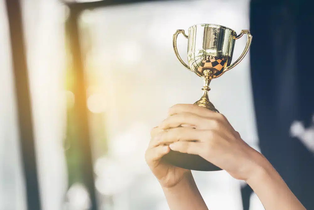 A woman holding up a trophy in front of a window.
