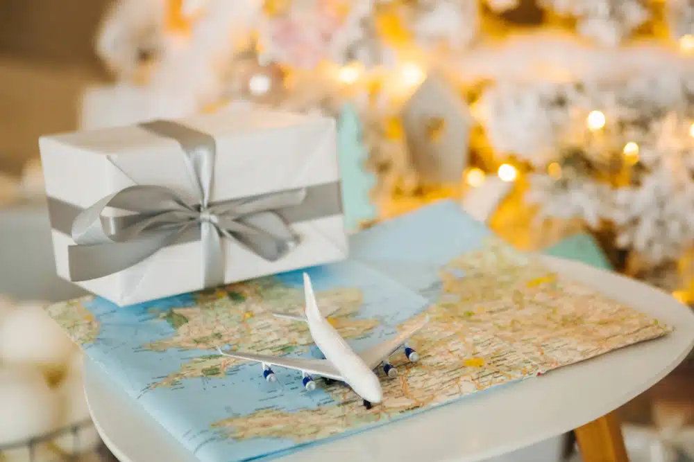 An American-themed gift box adorned with a plane and a map motif, placed next to a beautifully decorated Christmas tree.