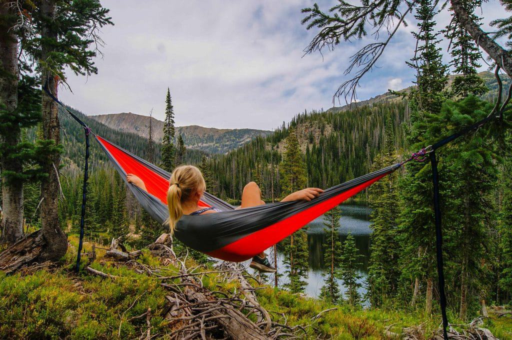 Enjoy a virtual tour of a woman peacefully laying in a hammock near a serene lake within the stunning views of a campground.