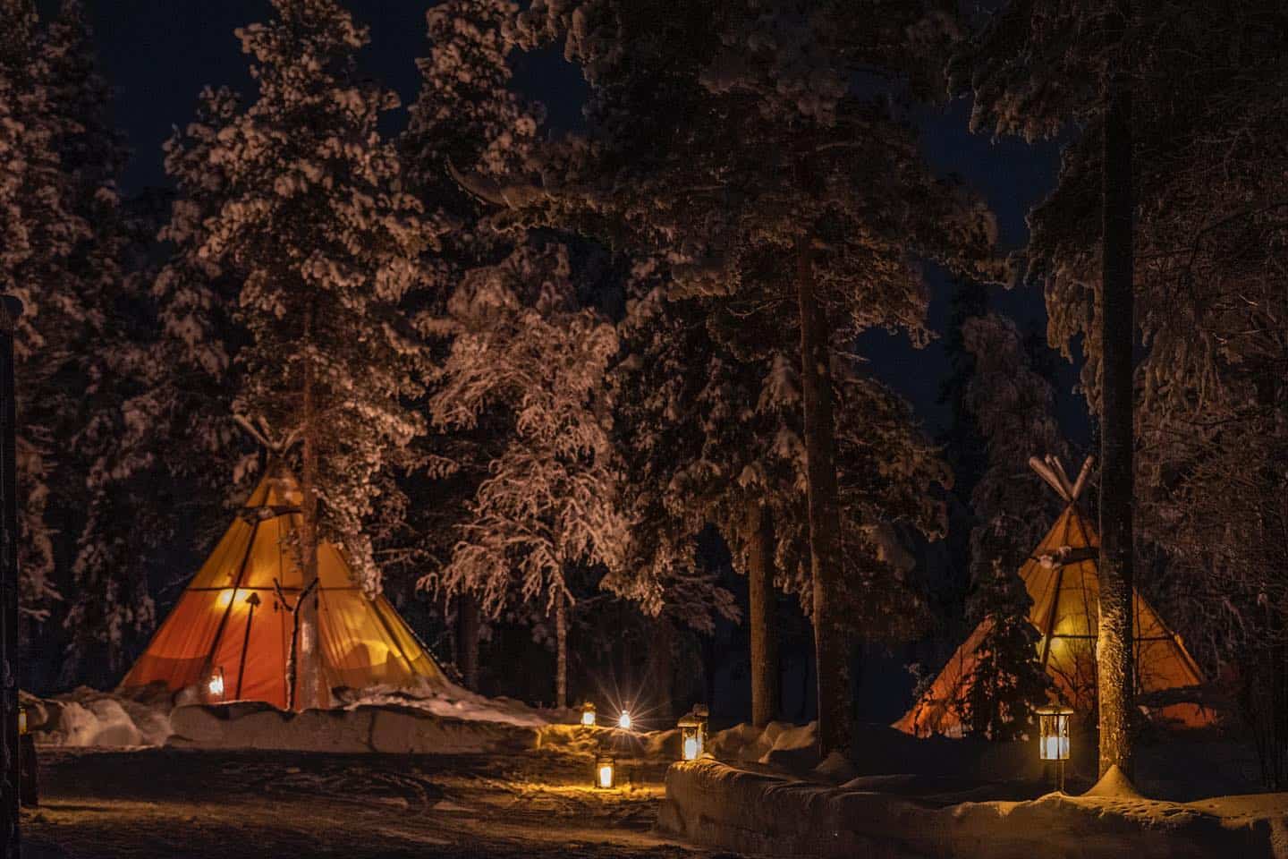 Two teepees lit up in the snow at night, inspired by Indigenous People of Northern Sweden's glamping experience.