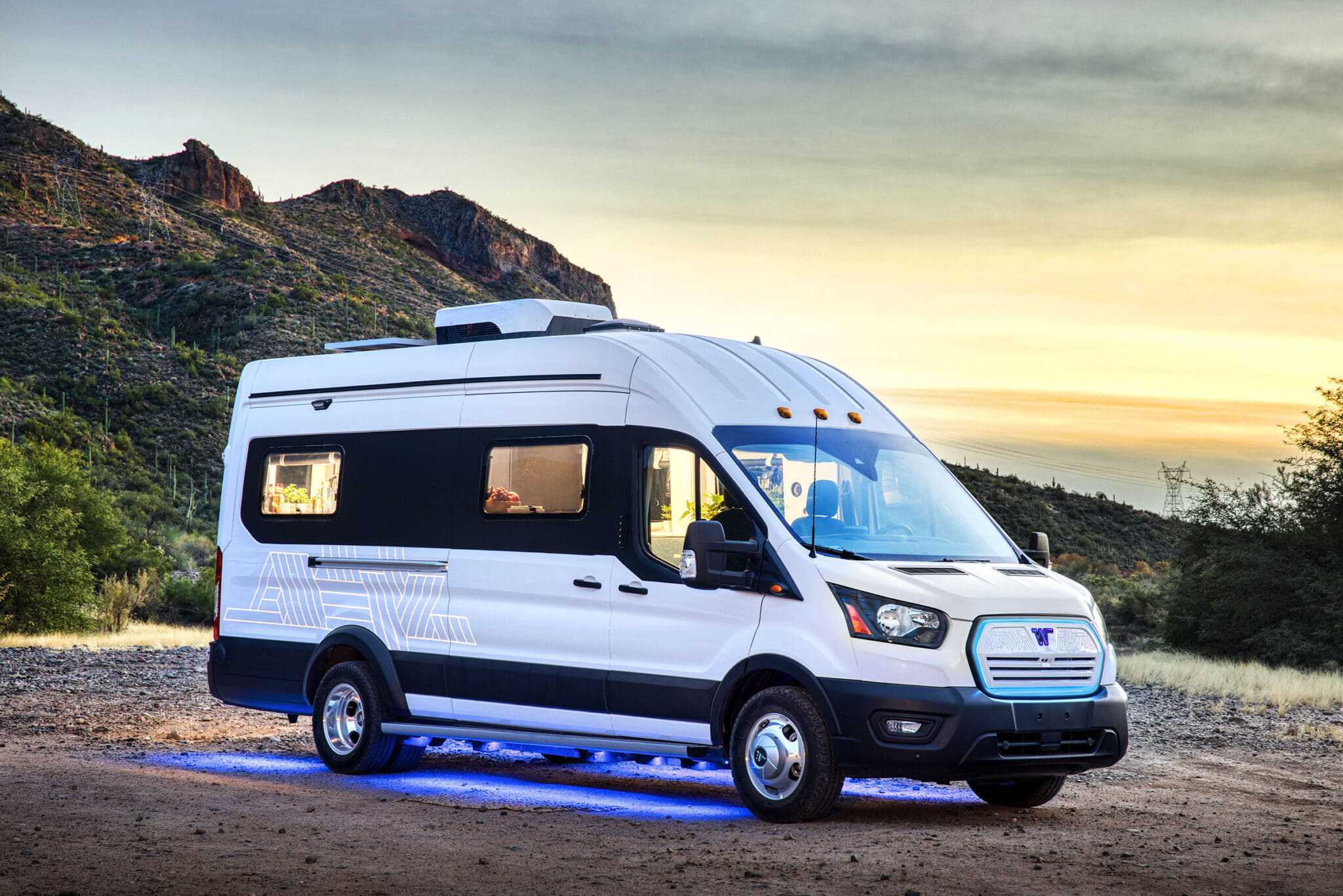 A white Winnebago Industries RV is parked on a dirt road, powered by an electric powertrain.