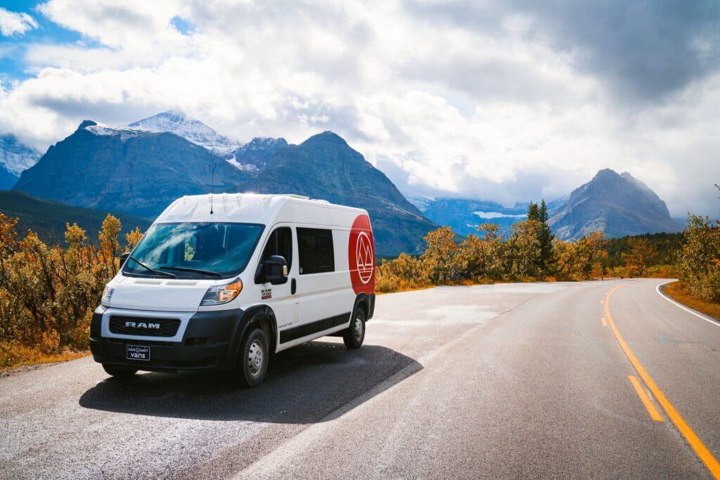 A white van from Dave & Matt Vans accelerates down a road with mountains in the background.