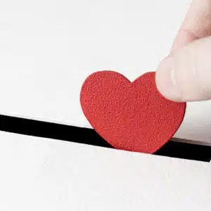 A hand putting a red heart into a box.