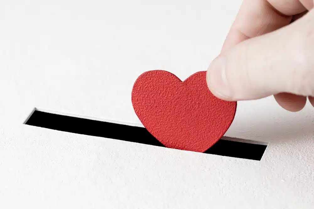 A hand putting a red heart into a box.