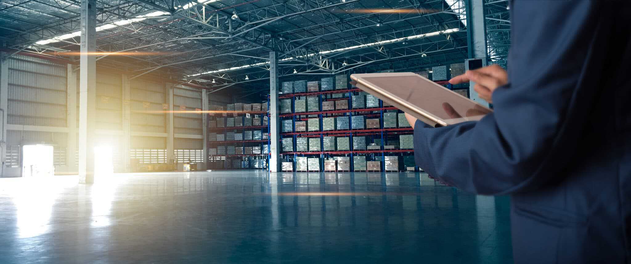 A man in a suit is holding a tablet in a warehouse, portraying an identity crisis within the US manufacturing industry.