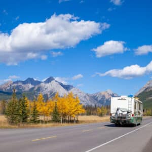 A rv traveling down a road with mountains in the background, showcasing the Canadian Outdoor Hospitality Conference and Expo scene.