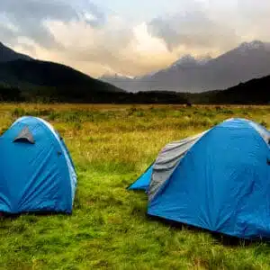 Two tents set up in a grassy field with mountains in the background, reminding campers of Auckland Council's freedom camping regulations.