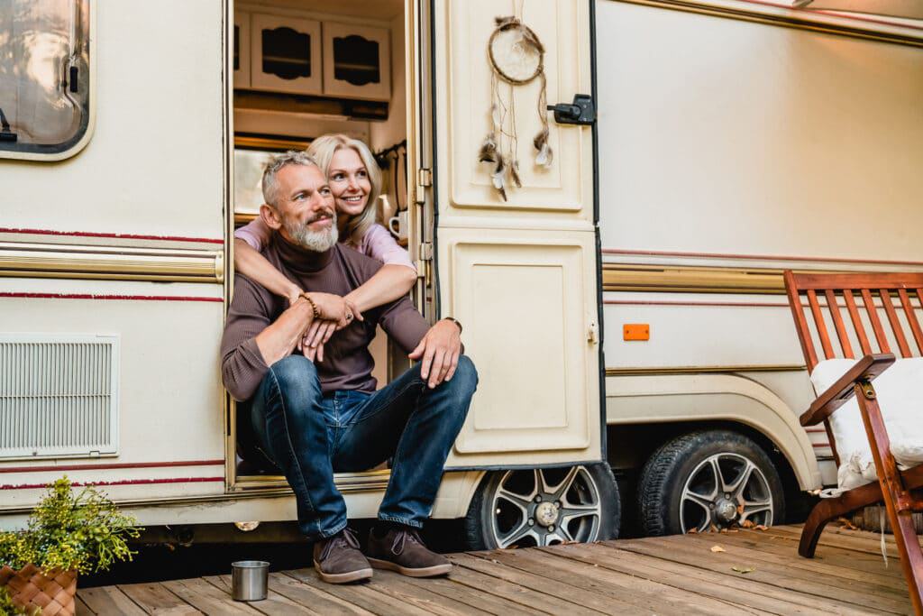 An Australian couple sitting on the porch of their RV at an overnight camping site.