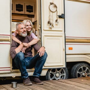 An Australian couple sitting on the porch of their RV at an overnight camping site.