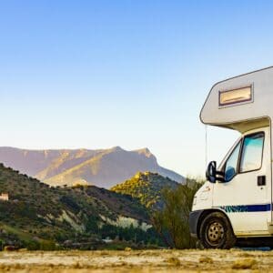 A white motorhome parked on a dirt road with mountains in the background.