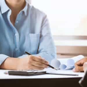A woman is sitting at a desk with a pen and paper.