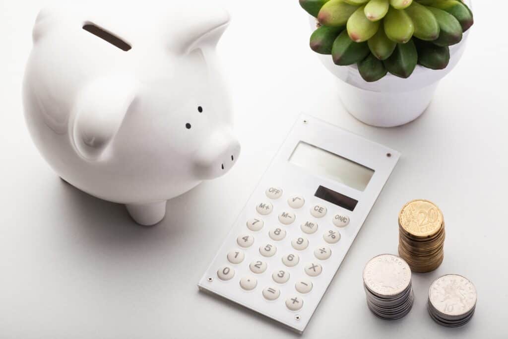 A piggy bank filled with coins sits next to a plant on a desk, while a calculator is used for digital financing calculations.