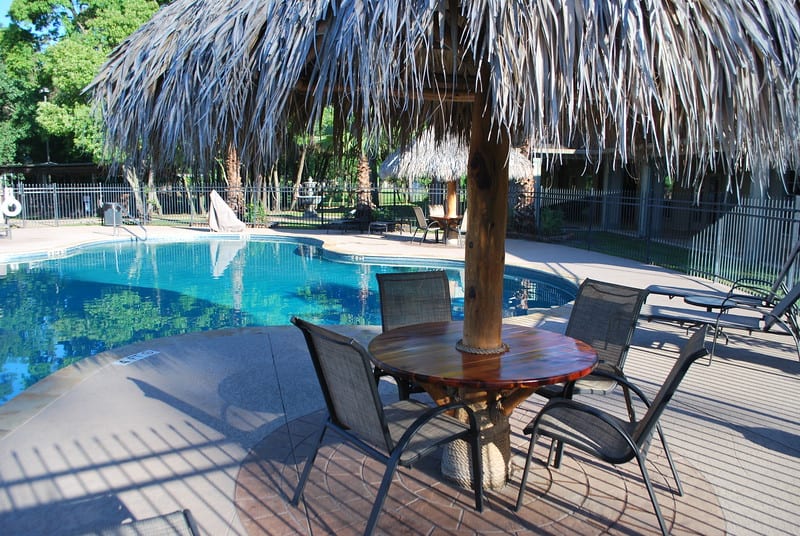 A spring break oasis with a pool and chairs under a thatched umbrella.