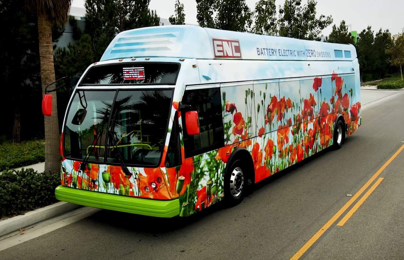 An ENC Battery Electric Zero-Emission Bus, adorned with vibrant flowers, is driving down the street.