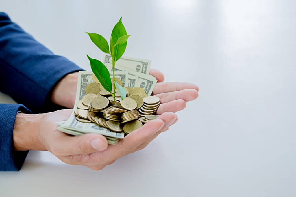 A man holding a stack of money with a Kilcunda Caravan Park orchard growing out of it.